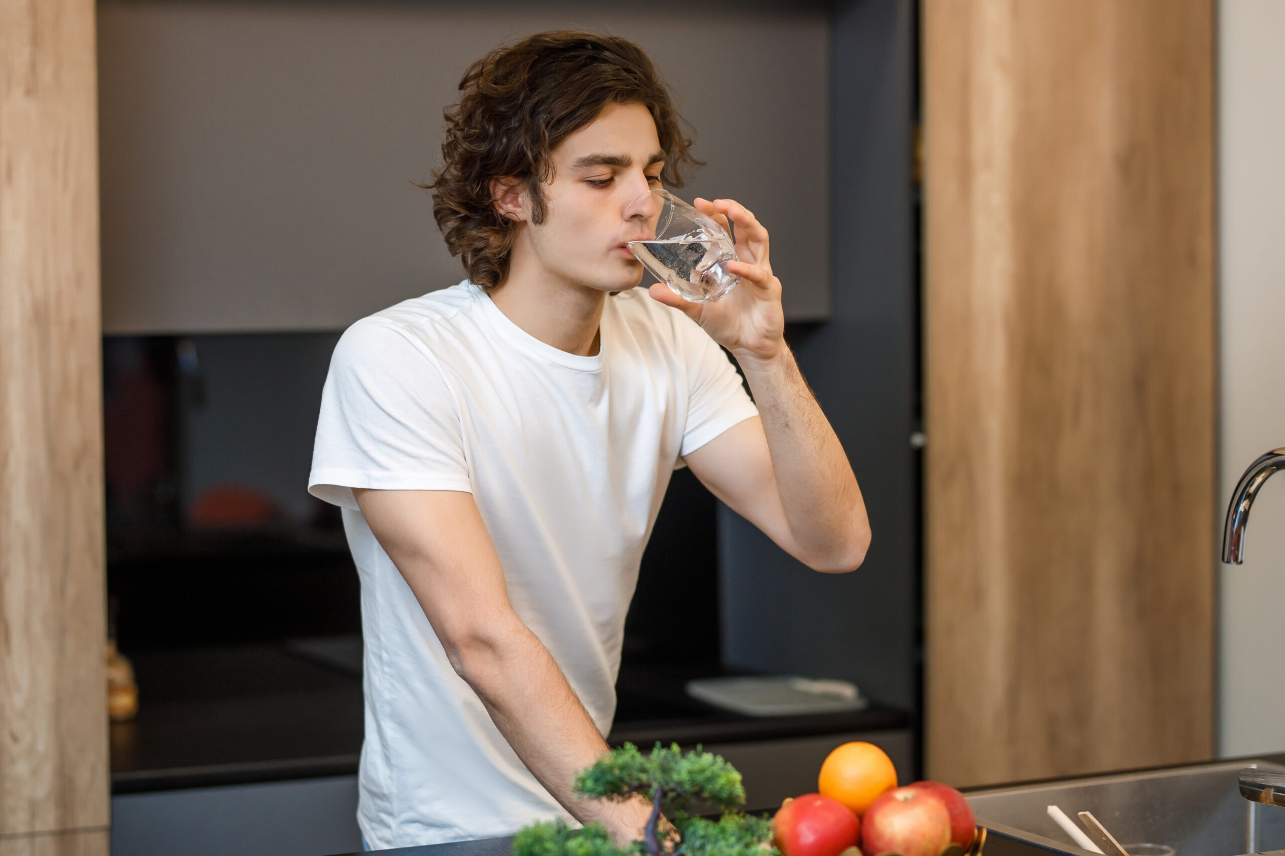 A person drinking a glass of clear, filtered water in a kitchen, illustrating building-grade water quality